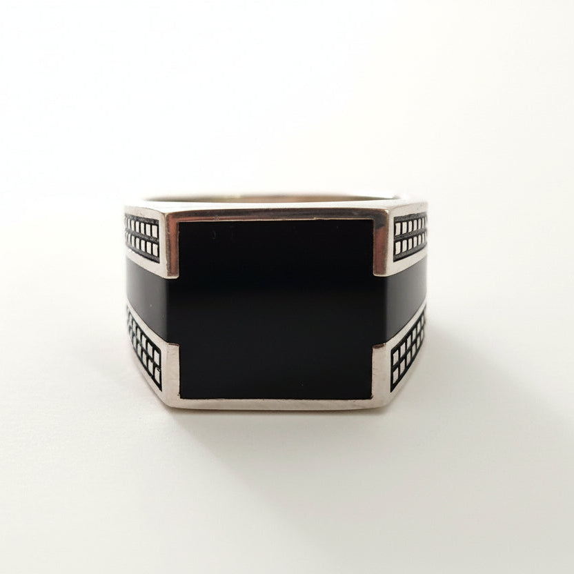 Silver ring with a black square center on a light gray background