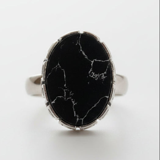 Ring with black marble-like stone and silver band on a gray background