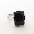 Silver ring with a black gemstone on a light gray background